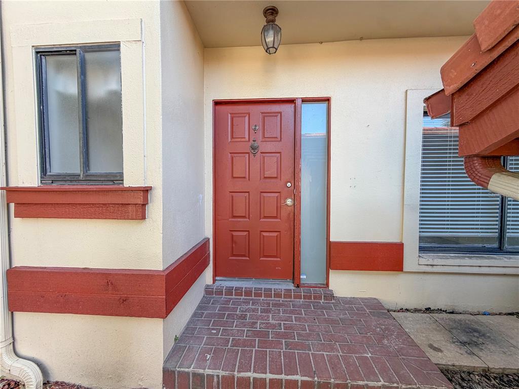 A red front door with a side window sits above a brick entryway — 3460 COUNTRYSIDE BOULEVARD UNIT 60, CLEARWATER, FL
