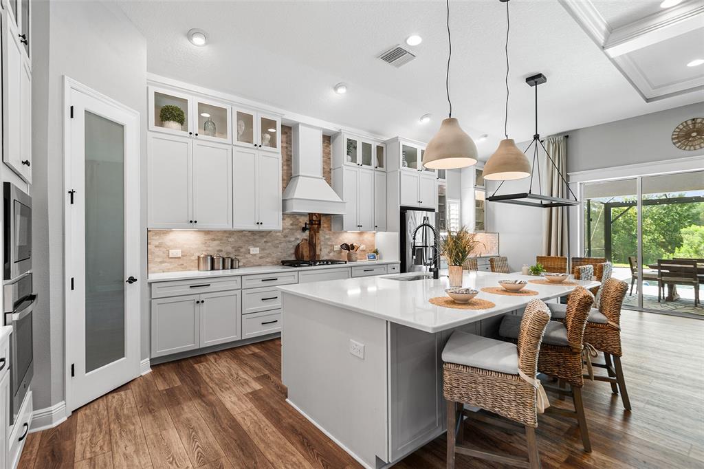 A modern kitchen features white cabinetry, a large quartz island, and wood-look flooring — 3994 WOODLAND RETREAT BOULEVARD, NEW PORT RICHEY, FL