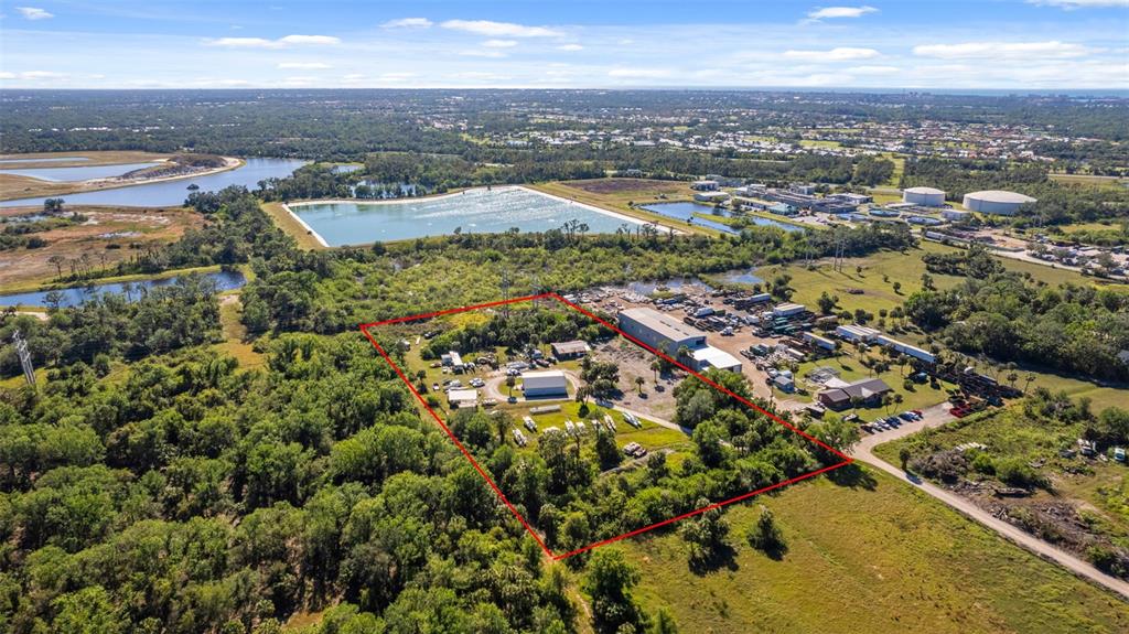 An aerial view shows a fenced industrial property with several buildings surrounded by dense trees — 3530 LAUREL ROAD E UNIT A, NORTH VENICE, FL