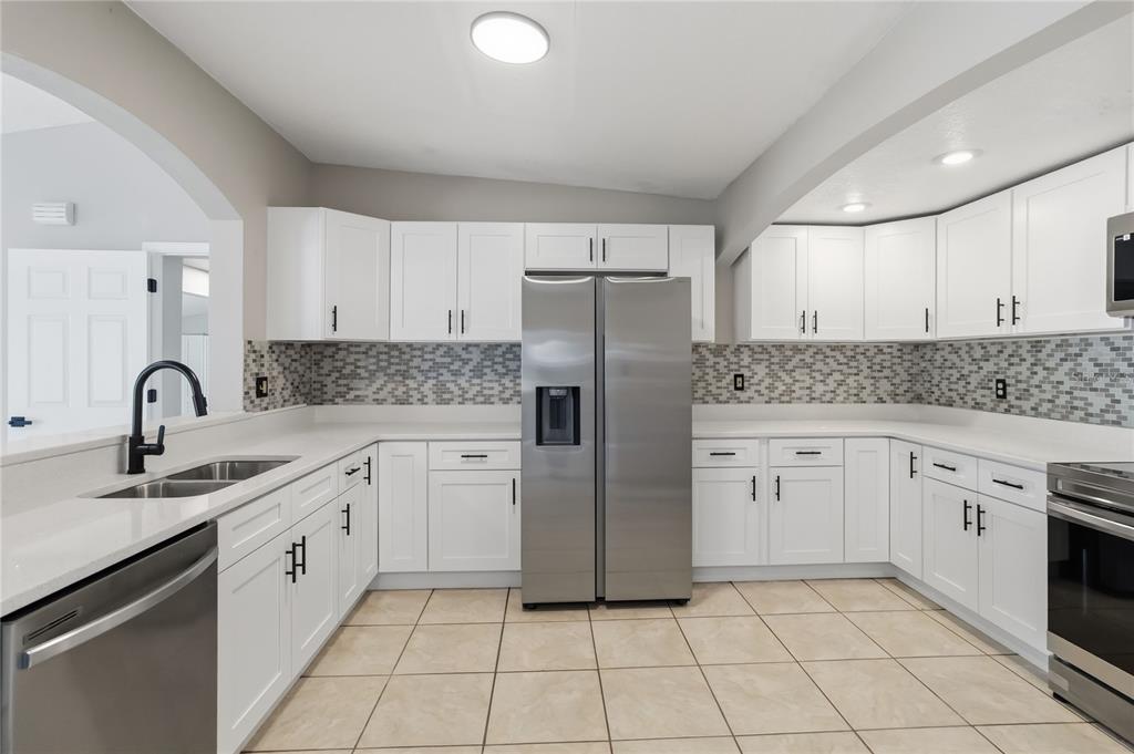 A kitchen with white cabinets, stainless steel appliances, a mosaic backsplash, and beige tile floors — 4870 LAKE CECILE DRIVE, KISSIMMEE, FL