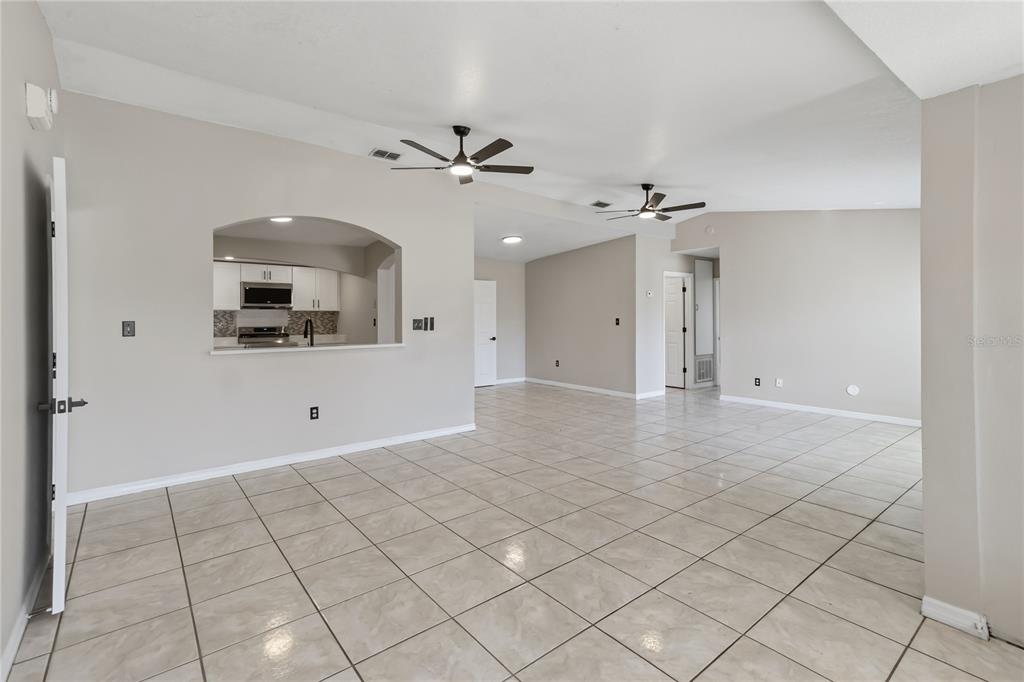An open-concept living area features light-colored tile flooring, two ceiling fans, and an arched kitchen pass-through — 4870 LAKE CECILE DRIVE, KISSIMMEE, FL