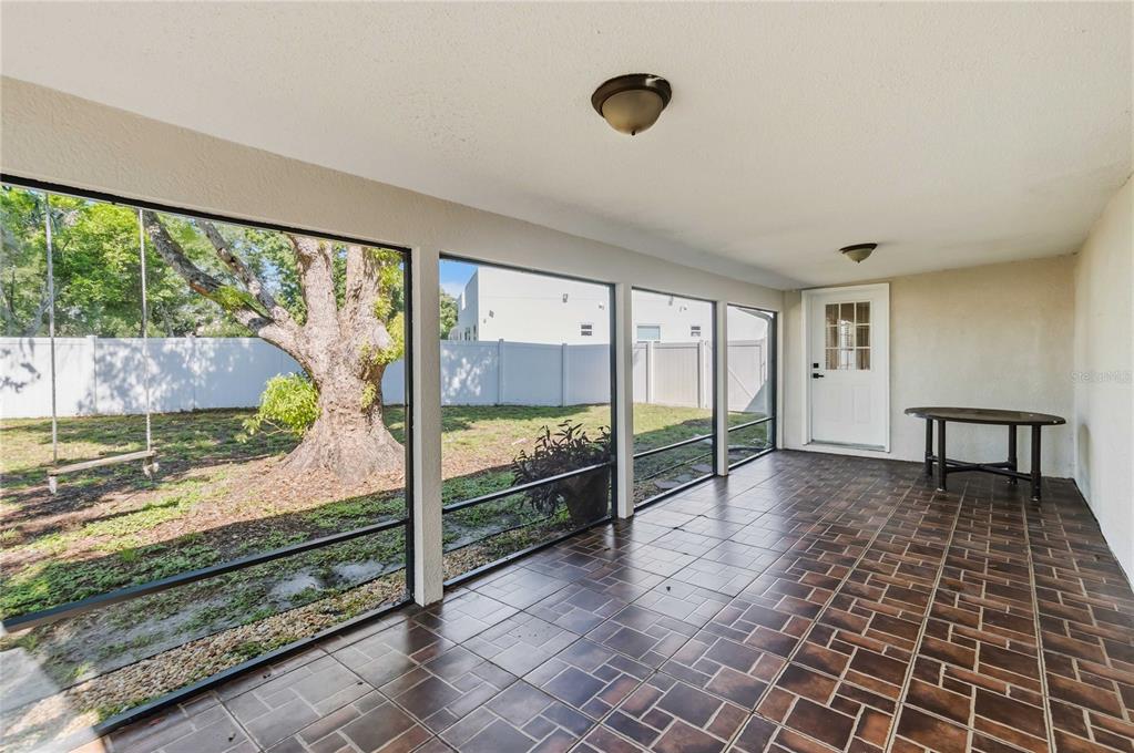 A screened-in porch with brown tiled flooring, a white door, and a view of a yard — 4870 LAKE CECILE DRIVE, KISSIMMEE, FL