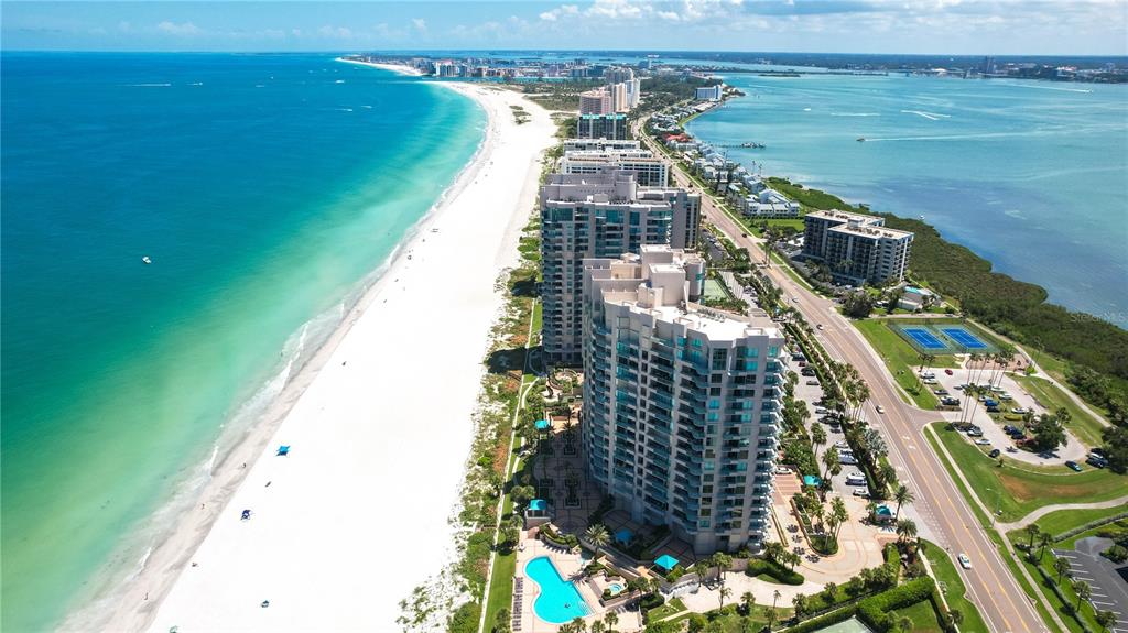 An aerial view shows high-rise condominiums situated between a white sand beach and a road — 1560 GULF BOULEVARD UNIT 1607, CLEARWATER, FL