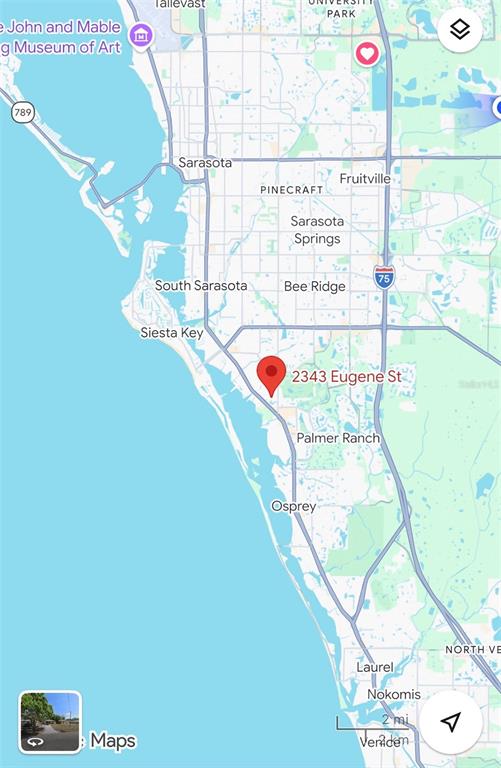 A wooden deck with outdoor furniture sits beside a white house under large trees — 2343 EUGENE STREET, SARASOTA, FL