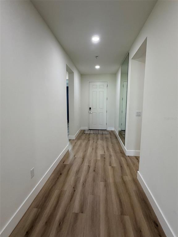 A hallway with light wood-look flooring leads to a white front door and a full-length mirror — 3467 74TH AVENUE CIRCLE E, SARASOTA, FL