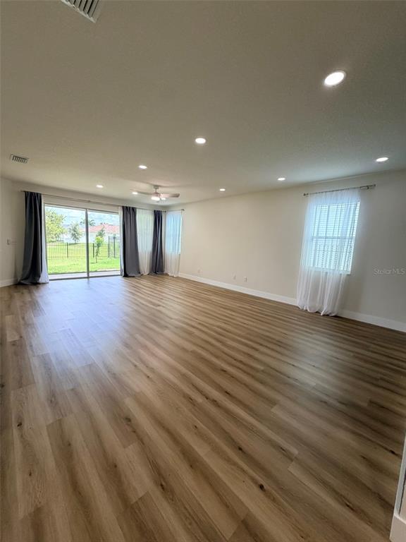 A spacious living room features light wood-look flooring, recessed lighting, and large sliding glass doors — 3467 74TH AVENUE CIRCLE E, SARASOTA, FL