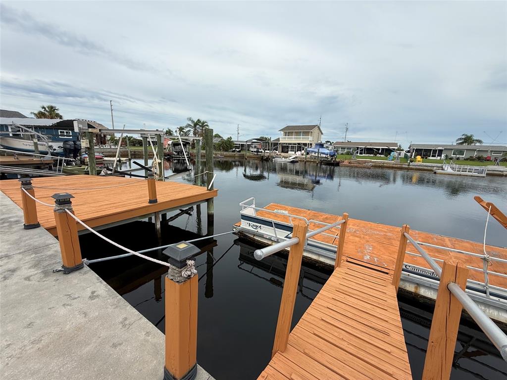 A wooden dock extends over a canal toward several houses under a cloudy sky — 12739 3RD ISLE, HUDSON, FL