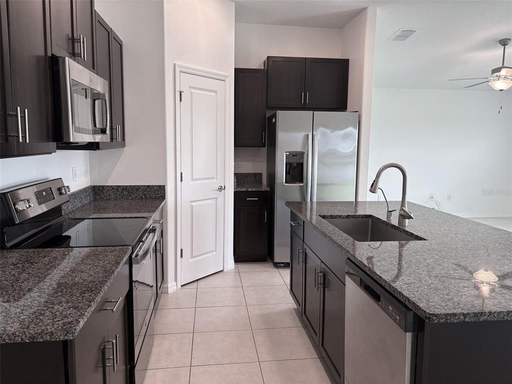 A kitchen features dark wood cabinets, granite countertops, stainless steel appliances, and a central island — 5487 BLUE AZURE DRIVE, WIMAUMA, FL