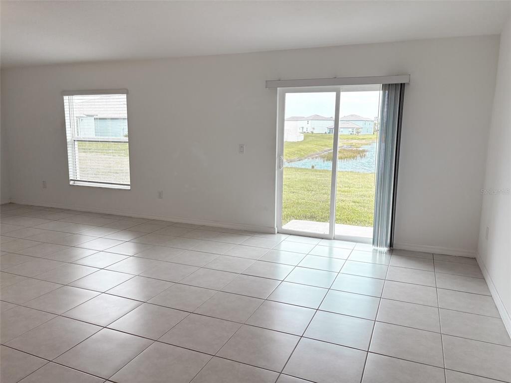 An empty room with light-colored tile flooring, a window, and a sliding glass door — 5487 BLUE AZURE DRIVE, WIMAUMA, FL