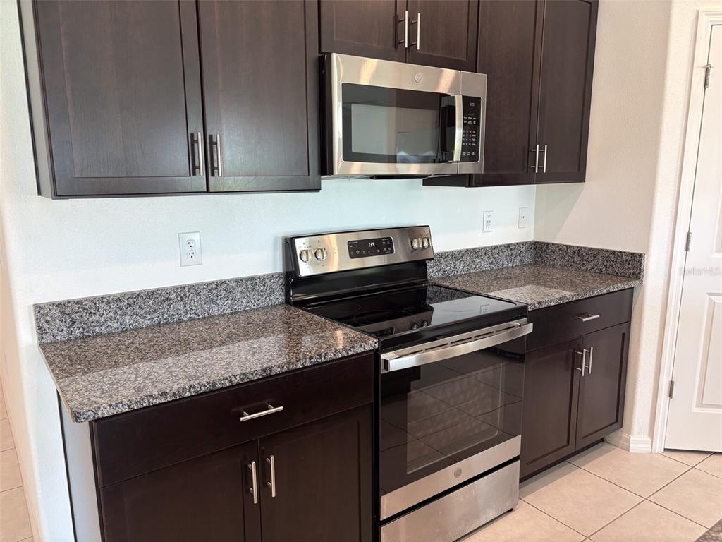A kitchen features dark wood cabinets, granite countertops, and stainless steel appliances — 5487 BLUE AZURE DRIVE, WIMAUMA, FL