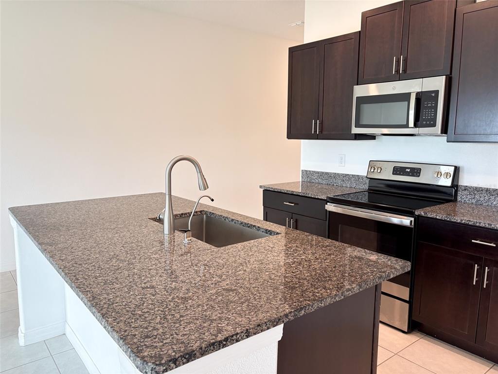 A kitchen features dark wood cabinets, granite countertops, a center island, and stainless steel appliances — 5487 BLUE AZURE DRIVE, WIMAUMA, FL