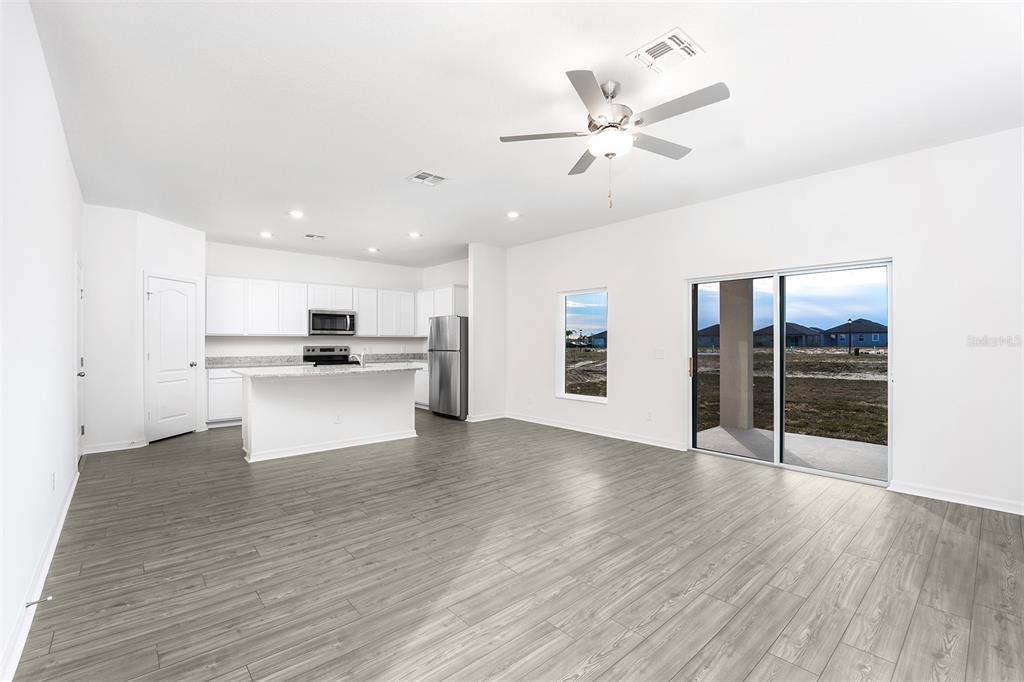 An open-concept kitchen and living area with white cabinets, stainless appliances, and gray wood flooring — 3808 CORSICAN PLACE, LAKE ALFRED, FL
