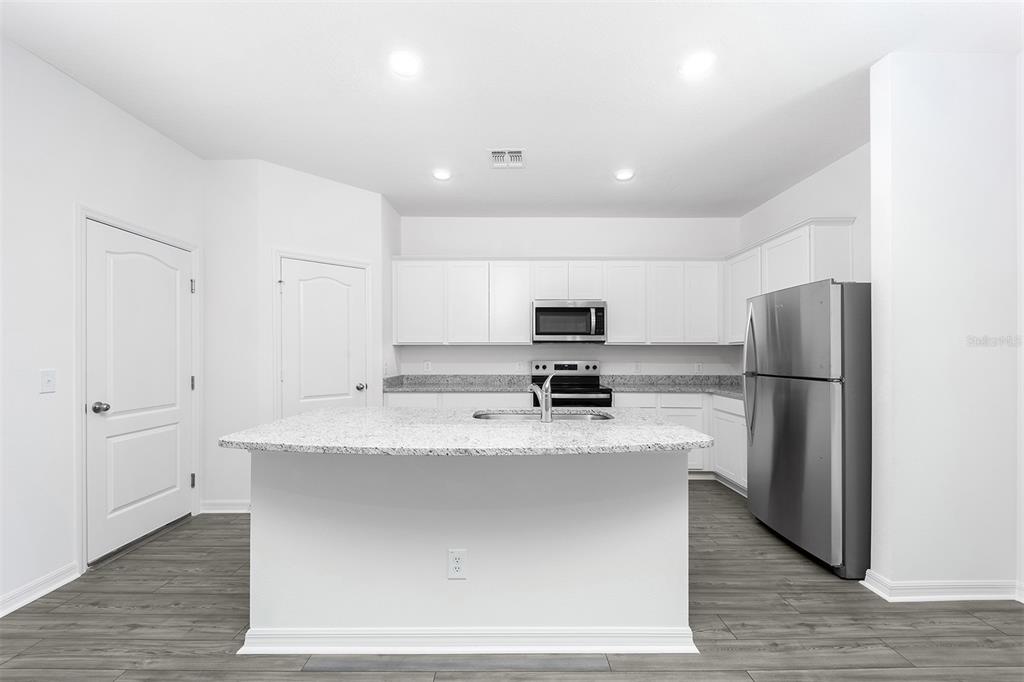 A kitchen featuring white cabinets, granite countertops, a center island, and stainless steel appliances — 3808 CORSICAN PLACE, LAKE ALFRED, FL