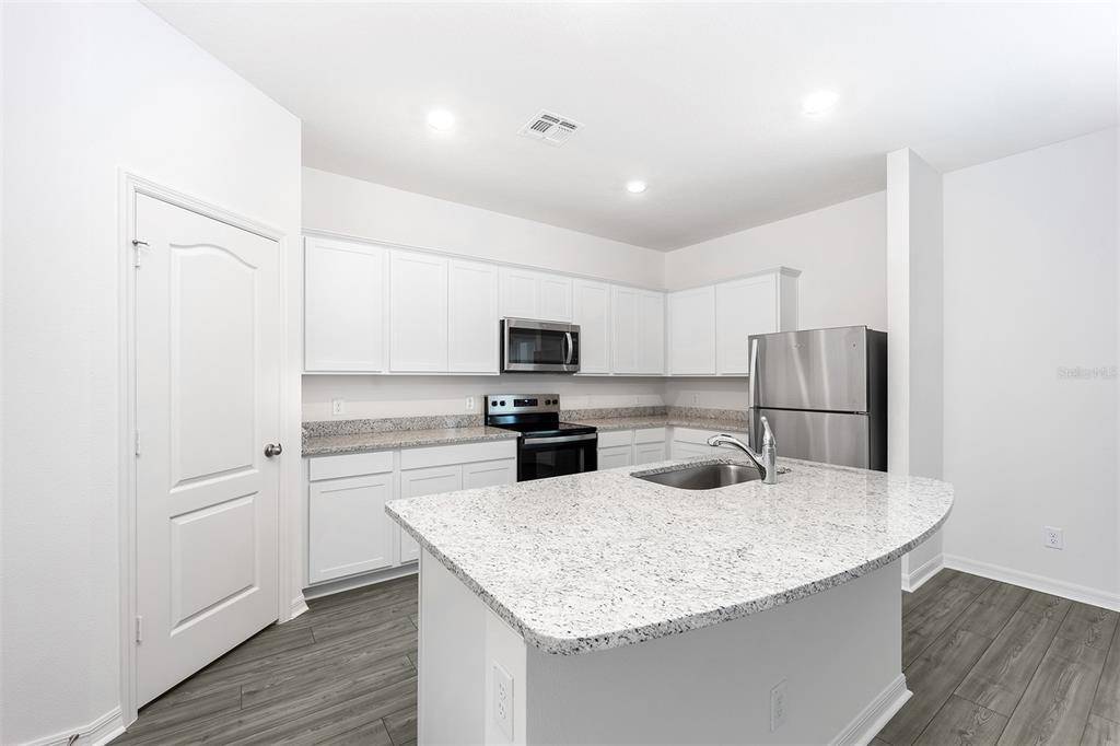 A modern kitchen features white cabinets, granite countertops, stainless steel appliances, and a central island — 3808 CORSICAN PLACE, LAKE ALFRED, FL