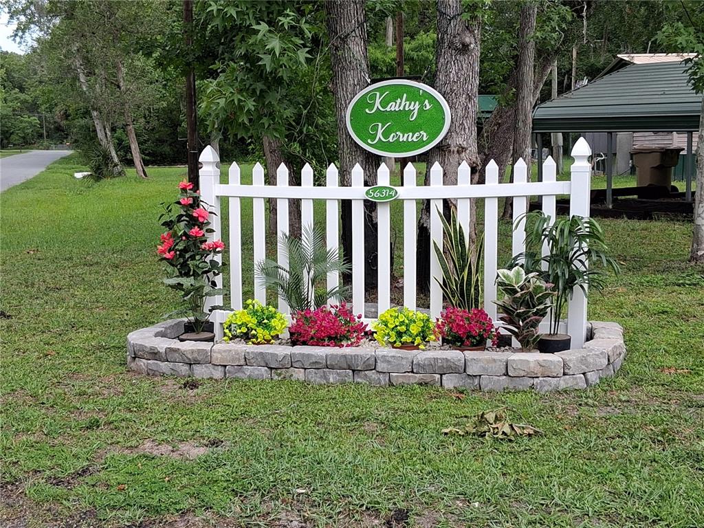 A white picket fence with potted flowers sits in front of a tree-lined yard — 56314 BLUE CREEK ROAD, ASTOR, FL