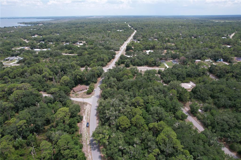 An aerial view shows a paved road winding through a wooded residential area — 1008 WILDFLOWER STREET, LAKE PLACID, FL