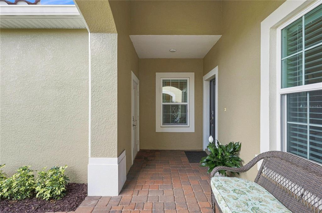 A covered entryway features a brick paver floor, a wicker bench, and a front door — 7201 VISTA BELLA DRIVE, BRADENTON, FL