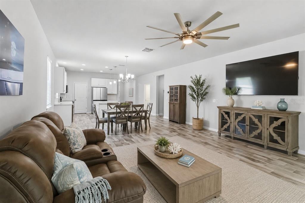 A living room with a brown sofa, coffee table, and television opens to a dining area — 12943 SATIN LILY DRIVE, RIVERVIEW, FL