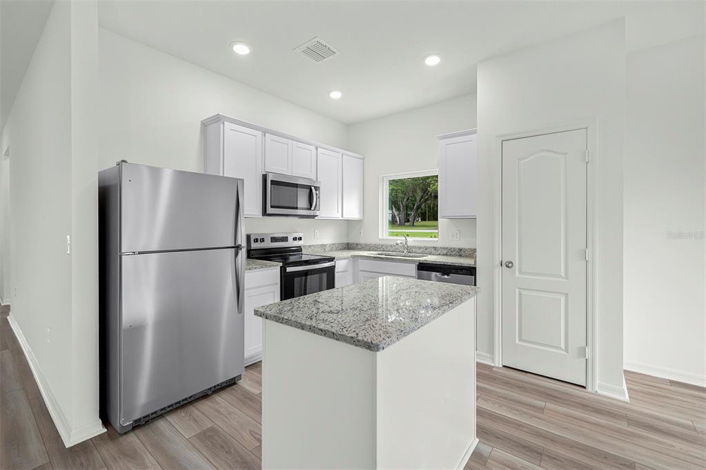 A kitchen features white cabinets, granite countertops, stainless steel appliances, and a central island — 13352 TULA LOOP, ASTATULA, FL