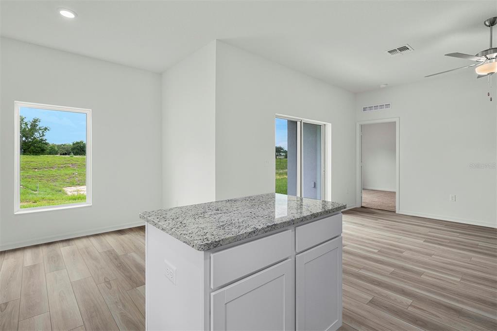 A kitchen island with a granite countertop sits in a room with light wood flooring — 13352 TULA LOOP, ASTATULA, FL