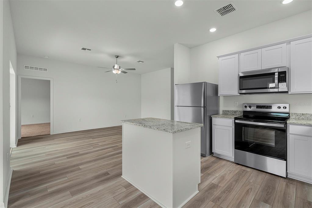 A kitchen with white cabinets, stainless steel appliances, and an island next to a room — 13352 TULA LOOP, ASTATULA, FL