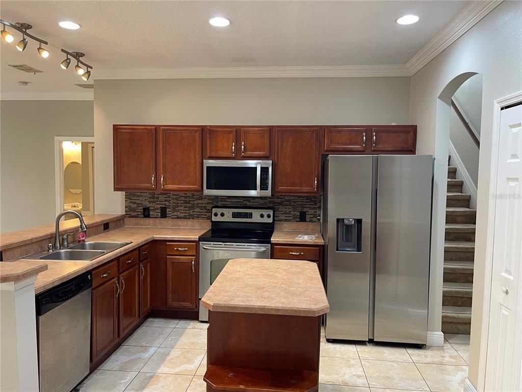 A kitchen features wood cabinets, stainless steel appliances, a center island, and tiled flooring — 3930 PORT SEA PLACE, KISSIMMEE, FL