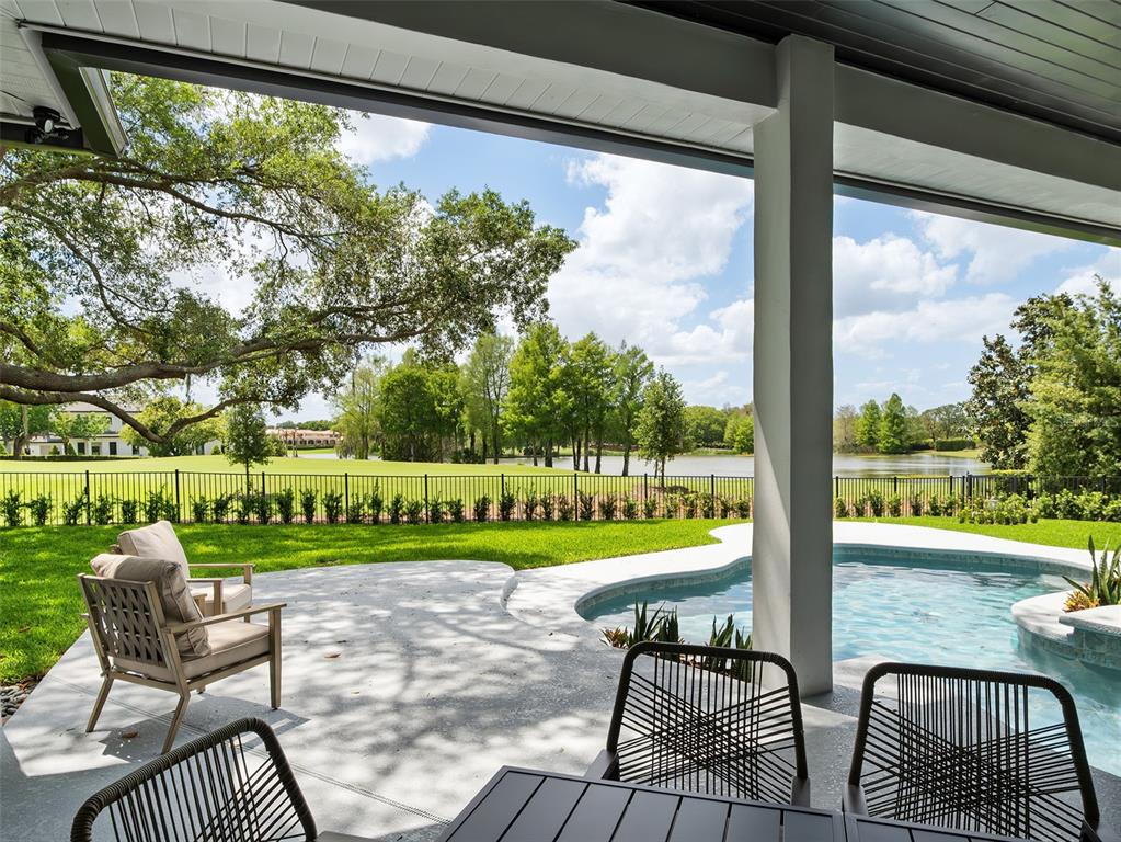 A covered patio overlooks a swimming pool, a fenced lawn, and a lake — 5138 FAIRWAY OAKS DR, WINDERMERE, FL