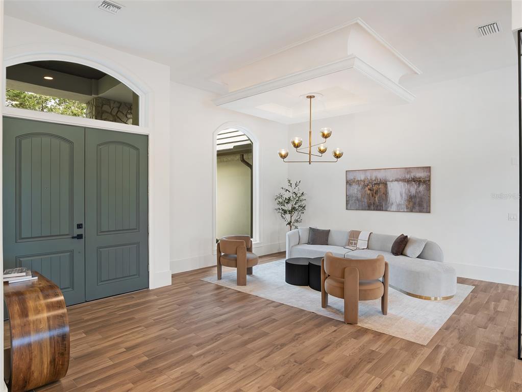 A bright living room features a green double door, wood flooring, and a modern chandelier — 5138 FAIRWAY OAKS DR, WINDERMERE, FL