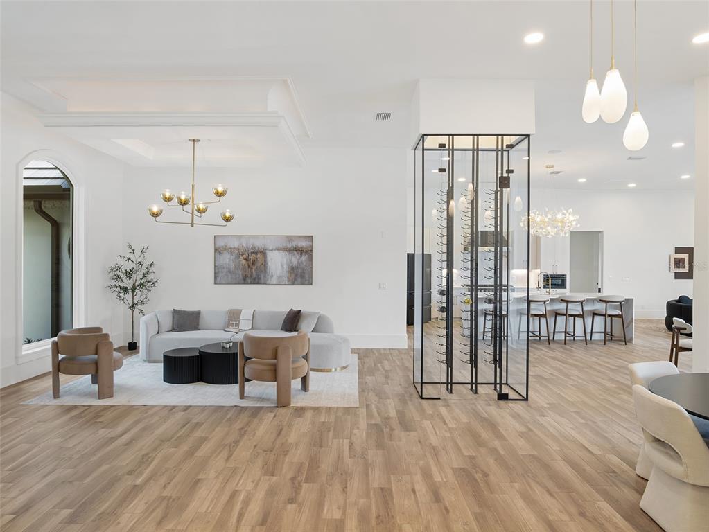 An open-concept living room features a glass-enclosed wine cellar, modern lighting, and wood-look flooring — 5138 FAIRWAY OAKS DR, WINDERMERE, FL