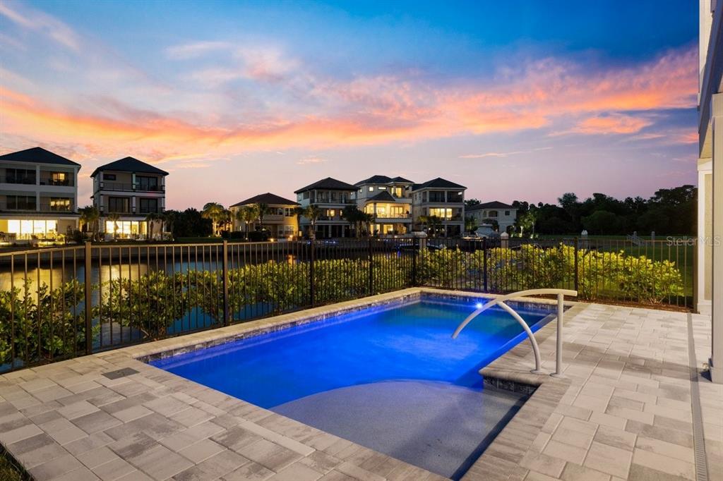A small rectangular swimming pool sits on a paved patio overlooking a canal and houses — 18 SPINAKER CIRCLE, PALM COAST, FL