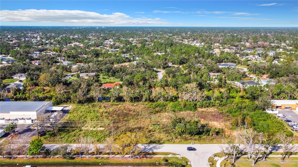 An aerial view shows a vacant, grassy lot situated between two commercial buildings and residential homes — 2725 COMMERCE PARKWAY, NORTH PORT, FL