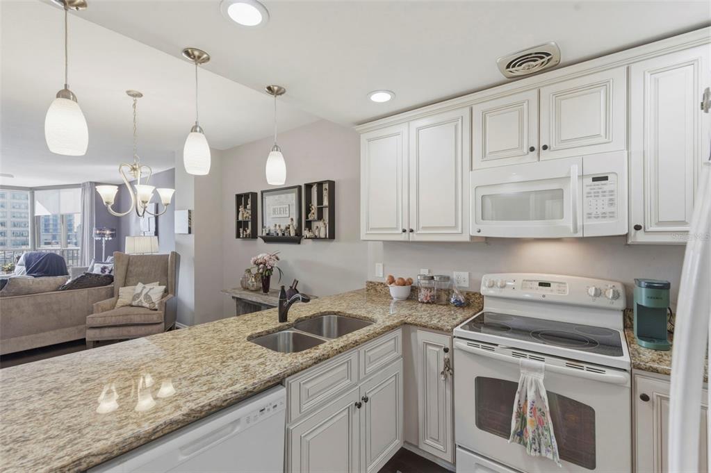 A kitchen with white cabinets, granite countertops, and a white stove overlooks a living area — 1 BEACH DRIVE SE UNIT 1109, ST PETERSBURG, FL