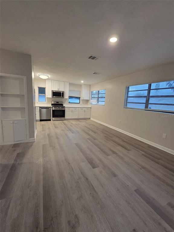 A kitchen with white cabinets and stainless steel appliances opens into a living area — 327 BARBARA CIRCLE, BELLEAIR, FL