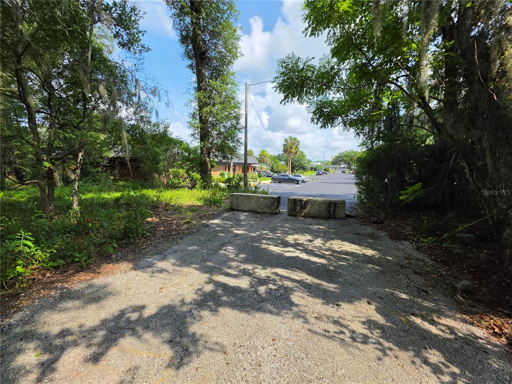 A gravel path leads to two concrete barriers blocking access to a paved parking lot — 0 WEST PLYMOUTH AVENUE, DELAND, FL