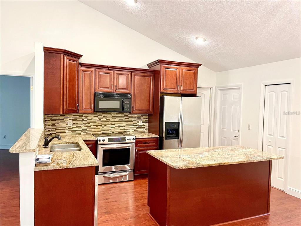 A kitchen with dark wood cabinets, granite countertops, stainless steel appliances, and wood-look flooring — 957 SOUTHRIDGE TRAIL, ALTAMONTE SPRINGS, FL