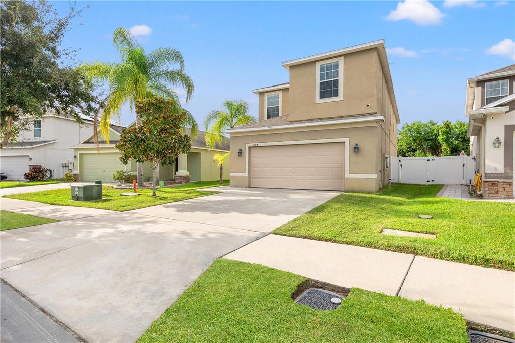 A two-story suburban house with a tan stucco exterior and a two-car garage — 1964 HAWKS VIEW DRIVE, RUSKIN, FL