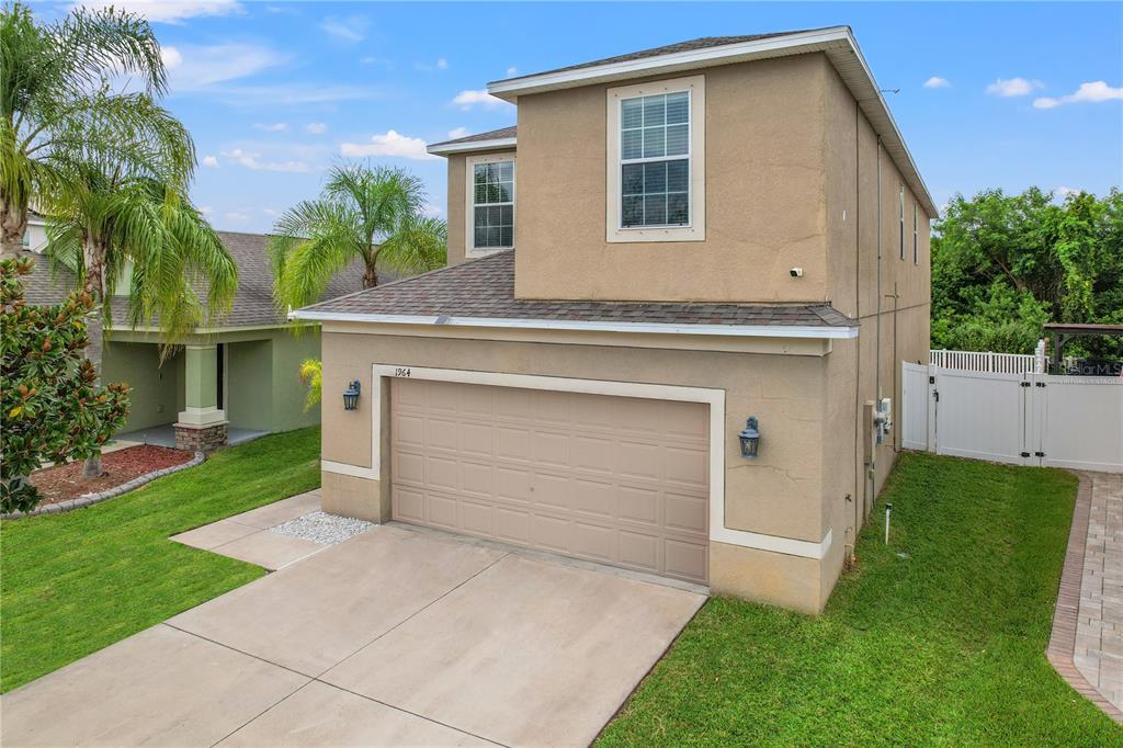 A two-story tan stucco house with a two-car garage and a white vinyl fence — 1964 HAWKS VIEW DRIVE, RUSKIN, FL