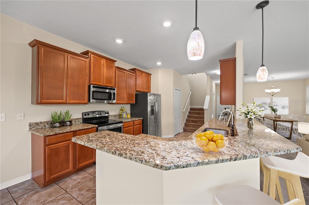 A kitchen with wood cabinets, granite countertops, and a breakfast bar overlooking a dining area — 1964 HAWKS VIEW DRIVE, RUSKIN, FL