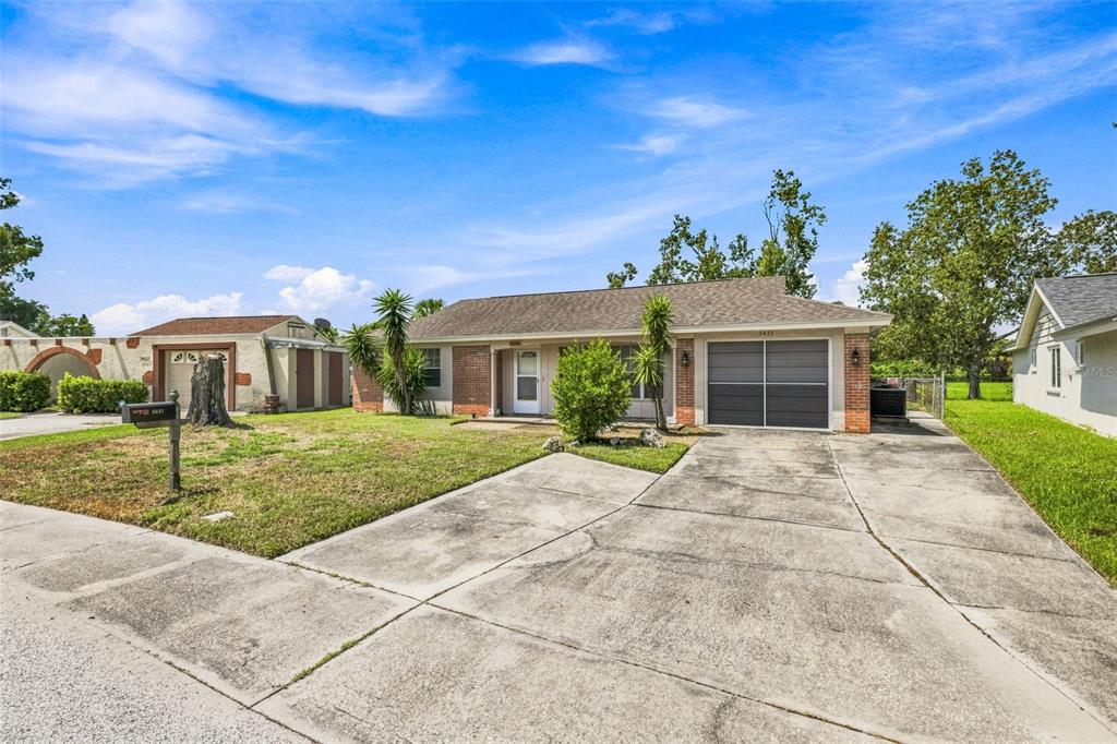 A single-story house with a concrete driveway, brick accents, and a garage under a blue sky — 3431 OVERLAND DRIVE, HOLIDAY, FL