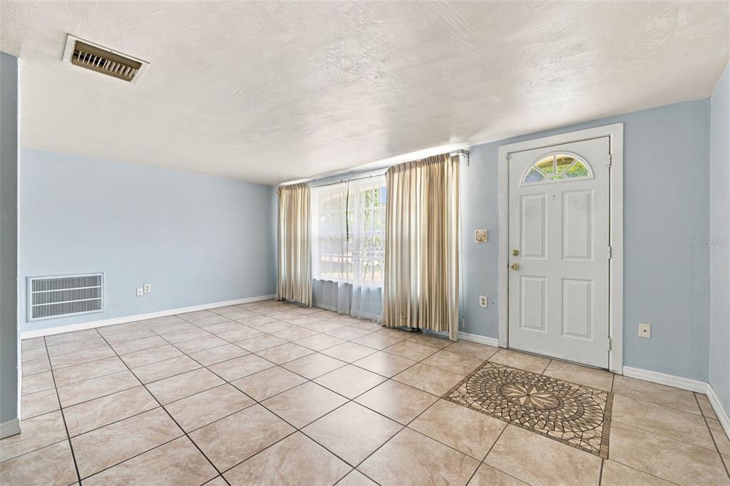 An empty room with light blue walls, beige tile flooring, and a white front door — 3431 OVERLAND DRIVE, HOLIDAY, FL
