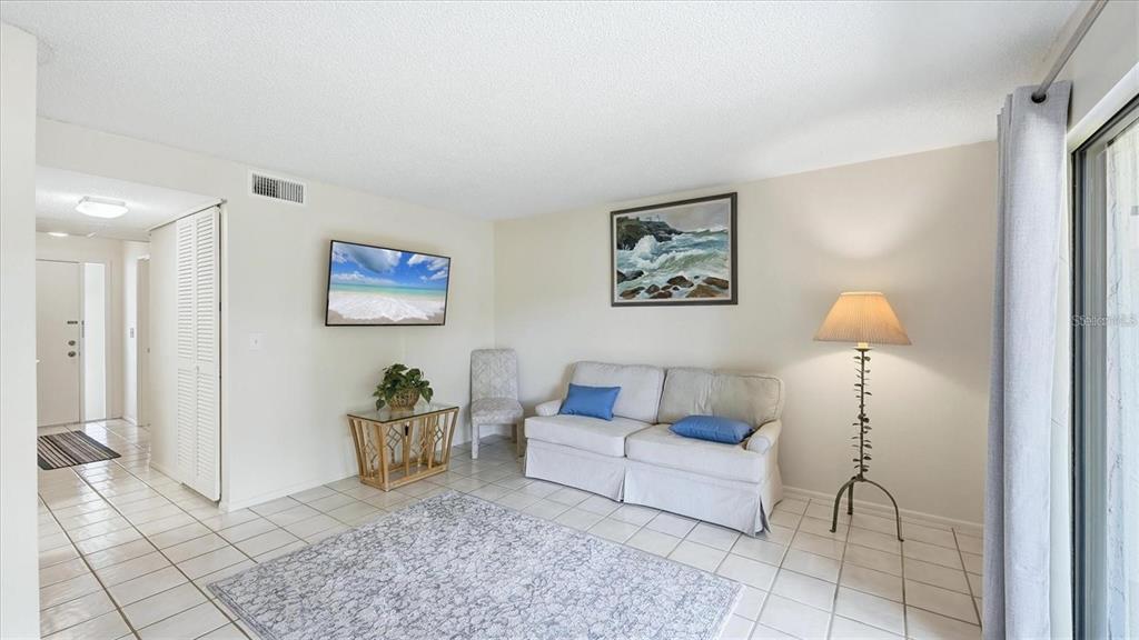 A living room features white tile floors, a light-colored sofa, a wall-mounted television, and a lamp — 3025 QUAIL HOLLOW UNIT 3025, SARASOTA, FL