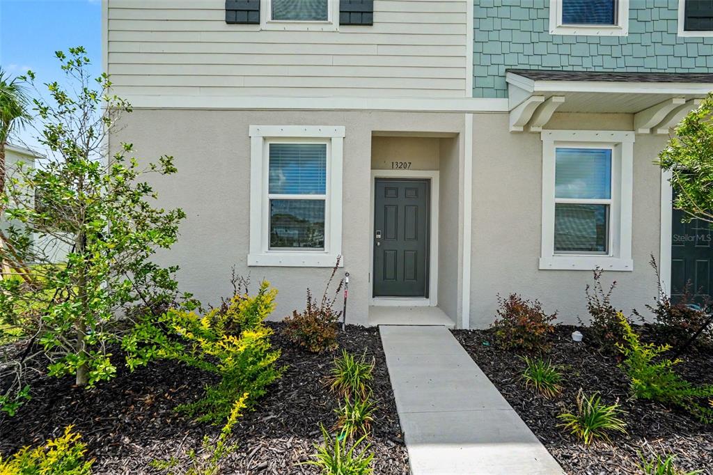 The exterior of a two-story townhouse features a gray front door and a concrete walkway — 13207 FORGE AVENUE, PARRISH, FL
