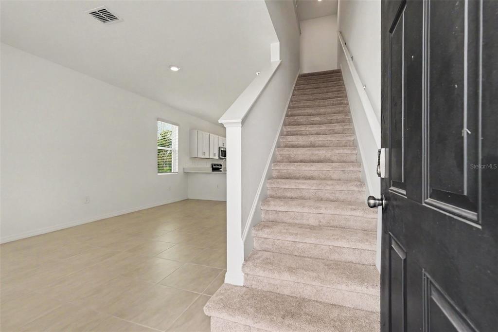An entryway features a carpeted staircase, tile flooring, and a view into a kitchen area — 13207 FORGE AVENUE, PARRISH, FL