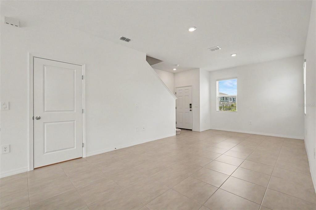 A bright, empty room features white walls, tile flooring, a staircase, and a front door — 13207 FORGE AVENUE, PARRISH, FL