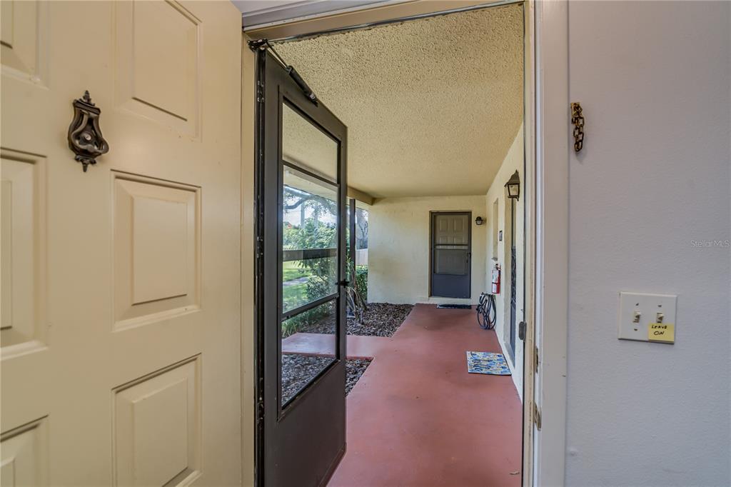 An open front door reveals a covered outdoor porch with a red concrete floor — 1119 9TH CIRCLE SE UNIT 1119, LARGO, FL