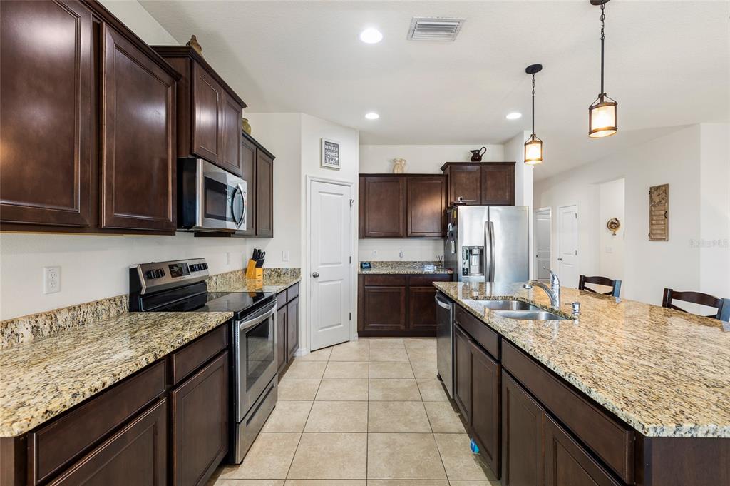 A kitchen with granite countertops, dark wood cabinets, and stainless steel appliances overlooks a dining area — 5025 JACKEL CHASE DRIVE, WIMAUMA, FL