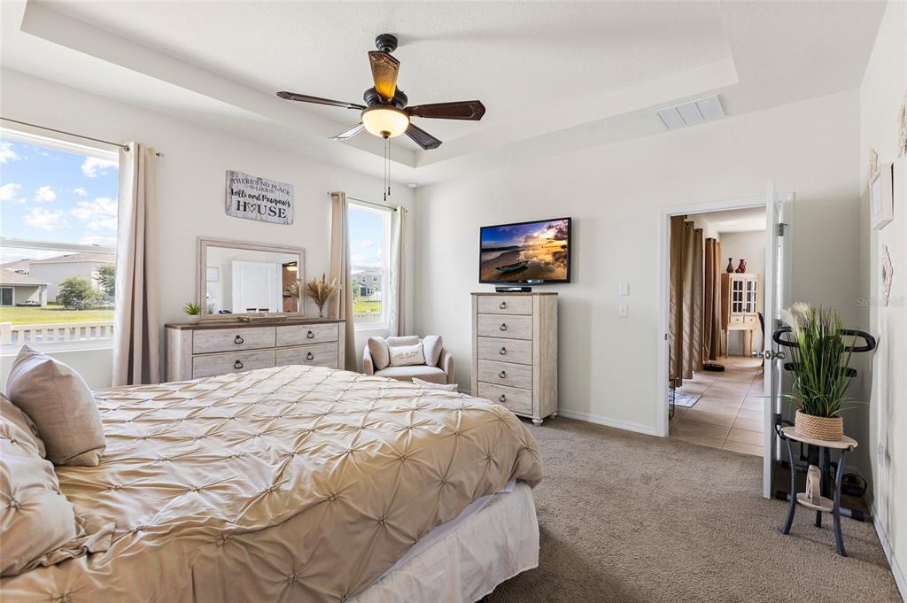 A bedroom features a bed, dresser, television, ceiling fan, and an open doorway to another room — 5025 JACKEL CHASE DRIVE, WIMAUMA, FL