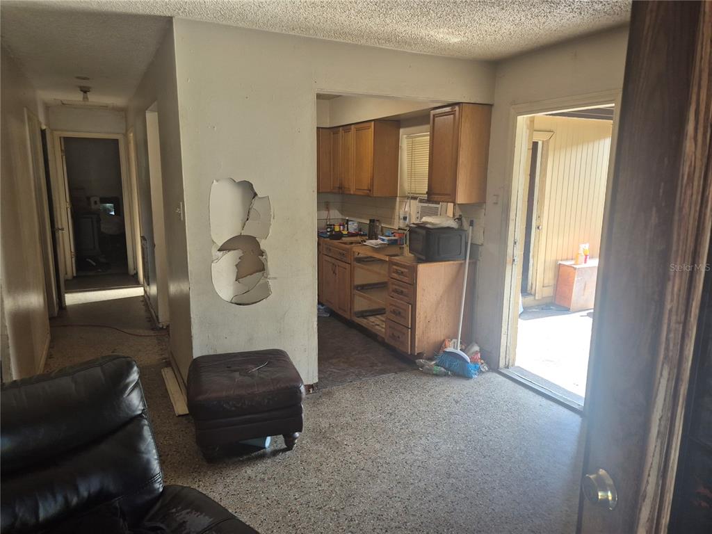 A living area with a damaged wall leads into a kitchen with wooden cabinets — 1909 W PALMETTO STREET, TAMPA, FL