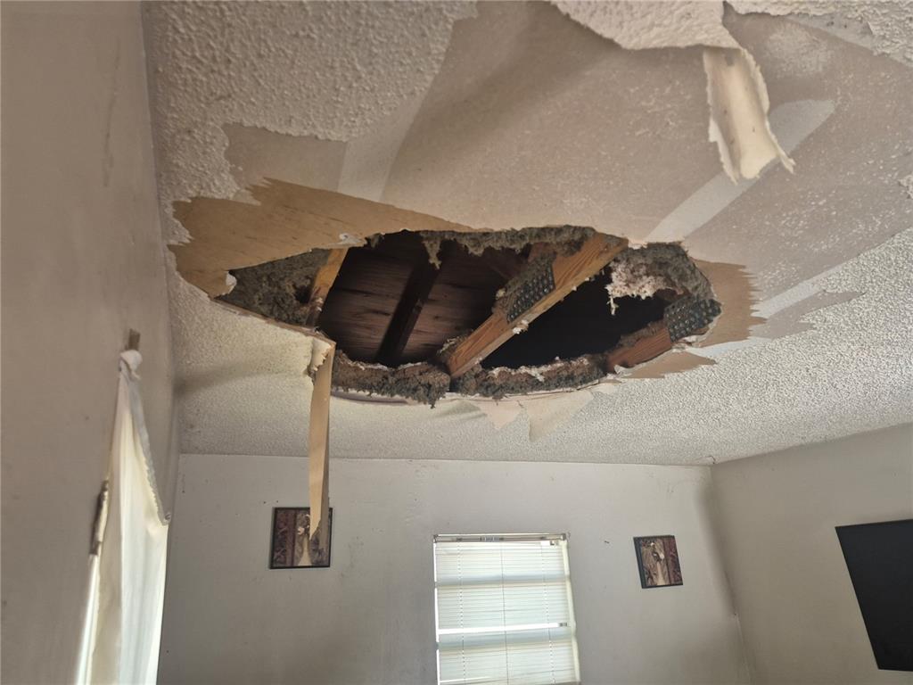 A room with a large hole in the popcorn-textured ceiling exposing the wooden roof structure — 1909 W PALMETTO STREET, TAMPA, FL