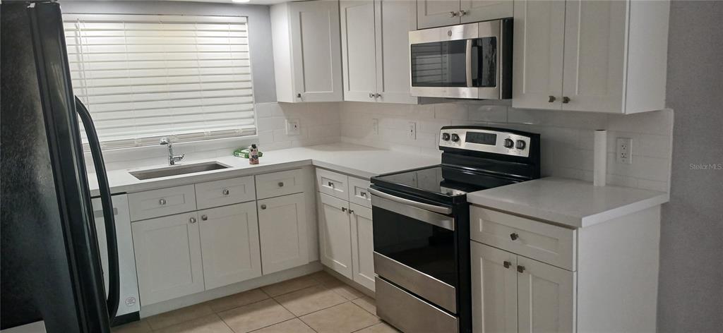 A kitchen with white cabinets and a dining area with a table and chairs — 1019 PENINSULA ROAD, TARPON SPRINGS, FL